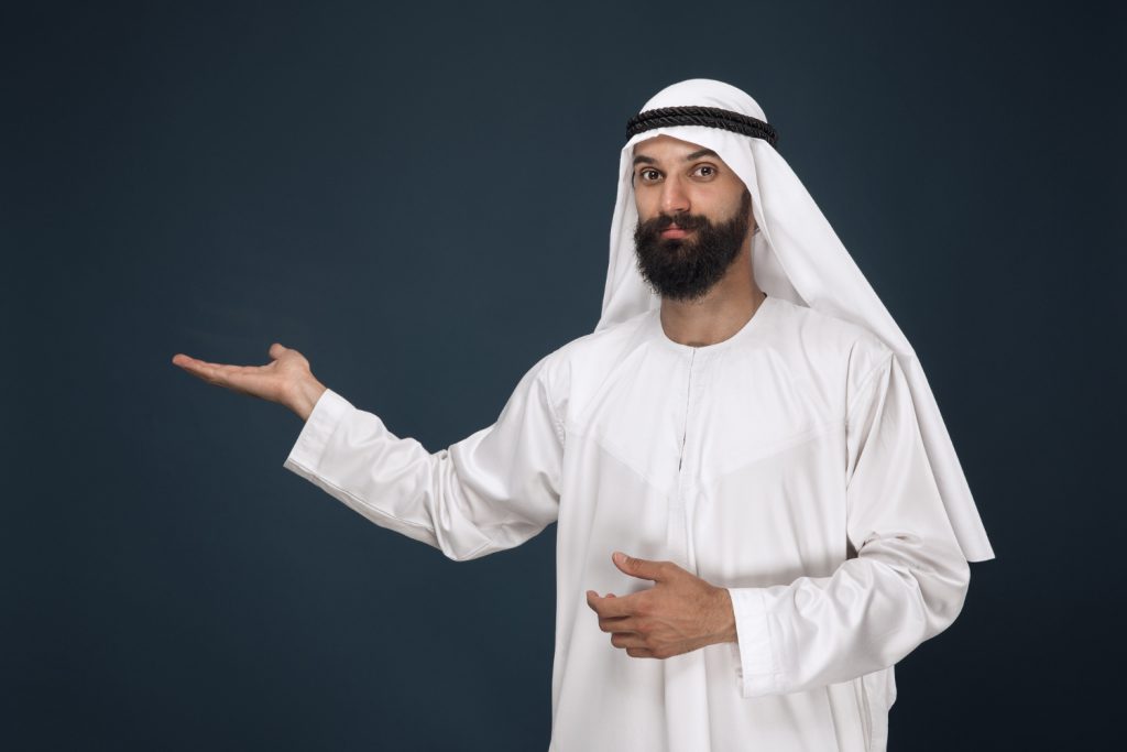 half length portrait arabian saudi man dark blue space young male model smiling pointing